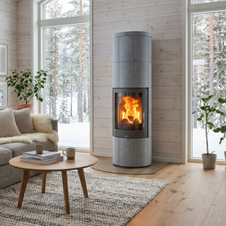 Täljstenskamin porto XL i ett modernt vardagsrum med brinnande eld och vinterlandskap utanför fönstret.